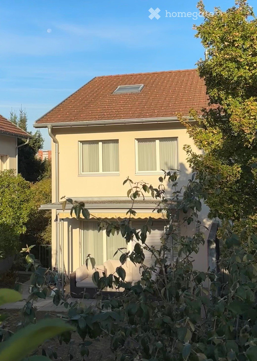 Two-story house with beige exterior, red-tiled roof, and covered patio area with outdoor seating.