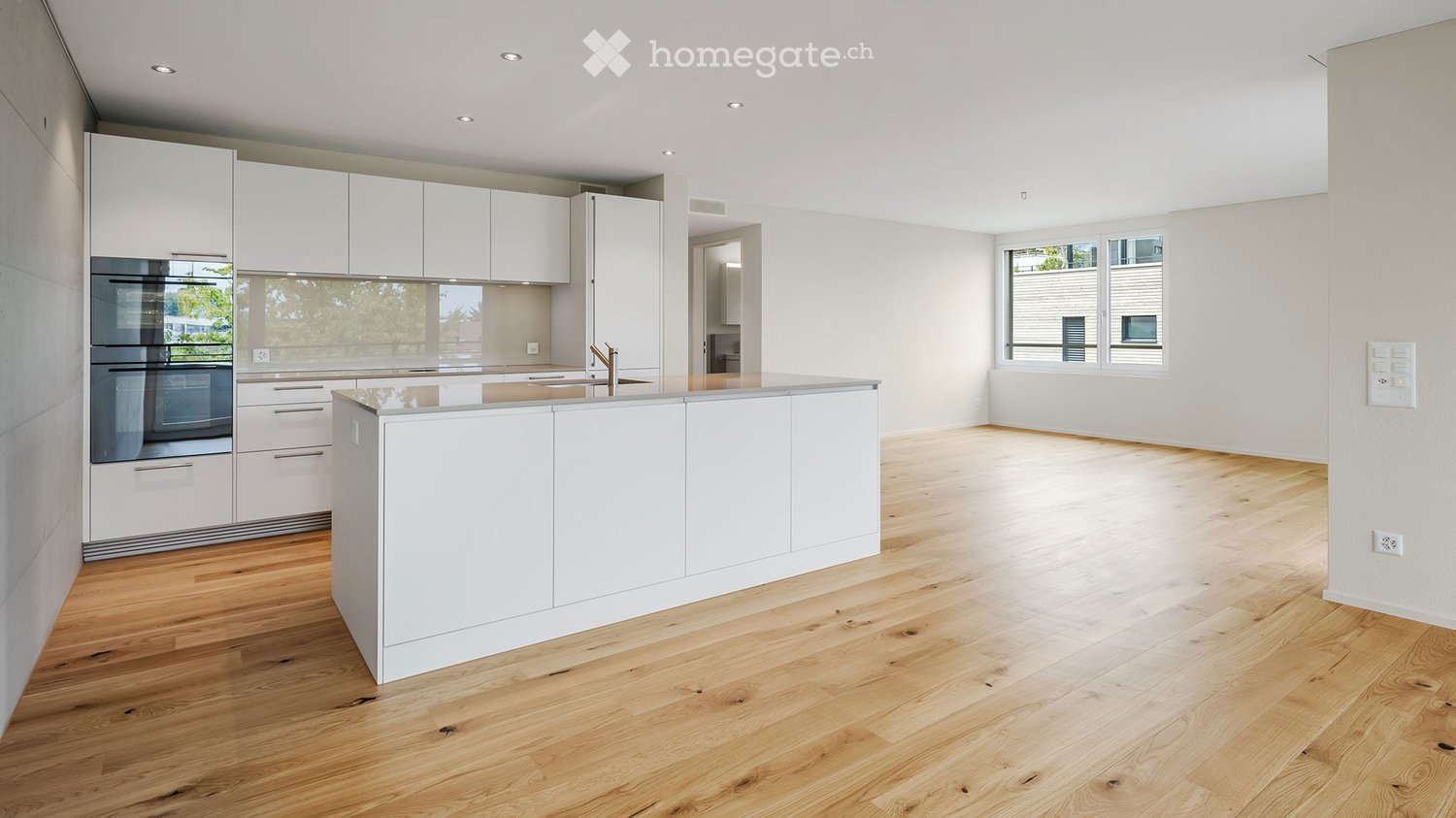 Modern kitchen with white cabinets, stainless steel oven, island, and wooden flooring.