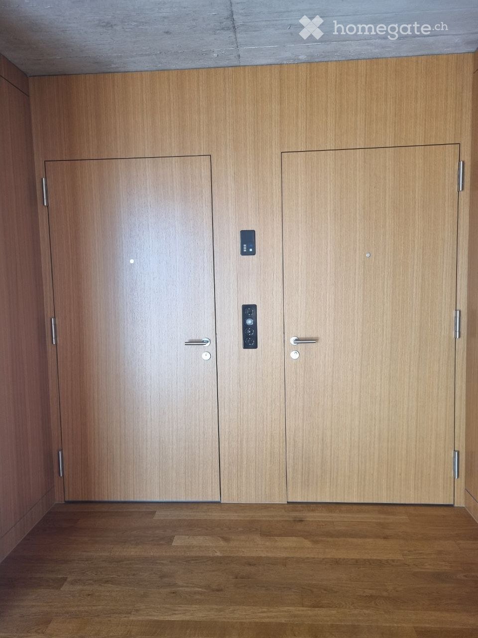 Empty hallway with wooden doors and a polished wooden floor, featuring modern door handles and a small control panel.