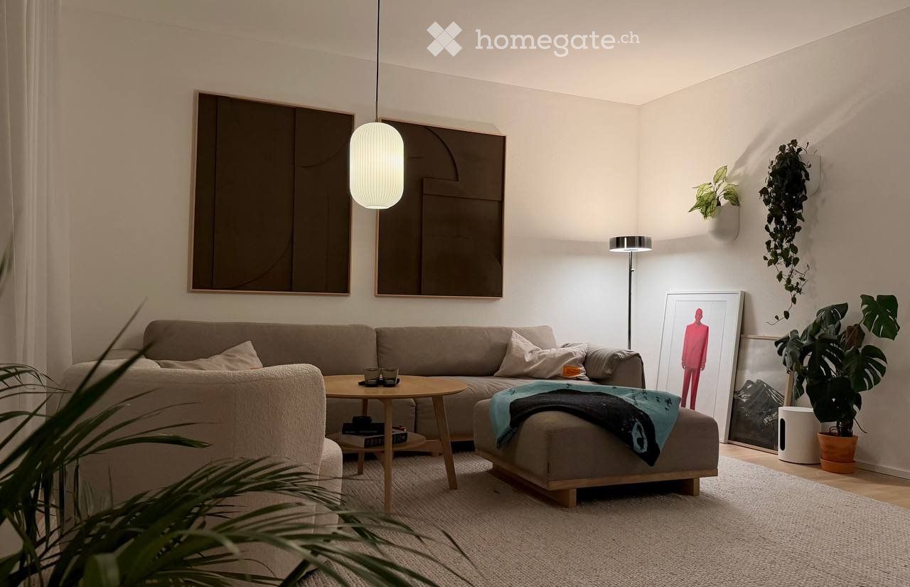 Modern living room with a grey sectional sofa, wooden coffee table, ottoman, floor lamp, and decorative art pieces.