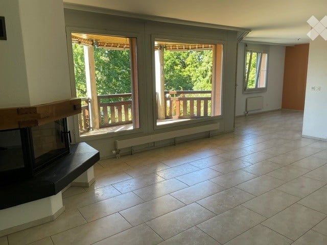 Empty living space with tiled flooring, large windows opening to a balcony, and a fireplace against one wall.