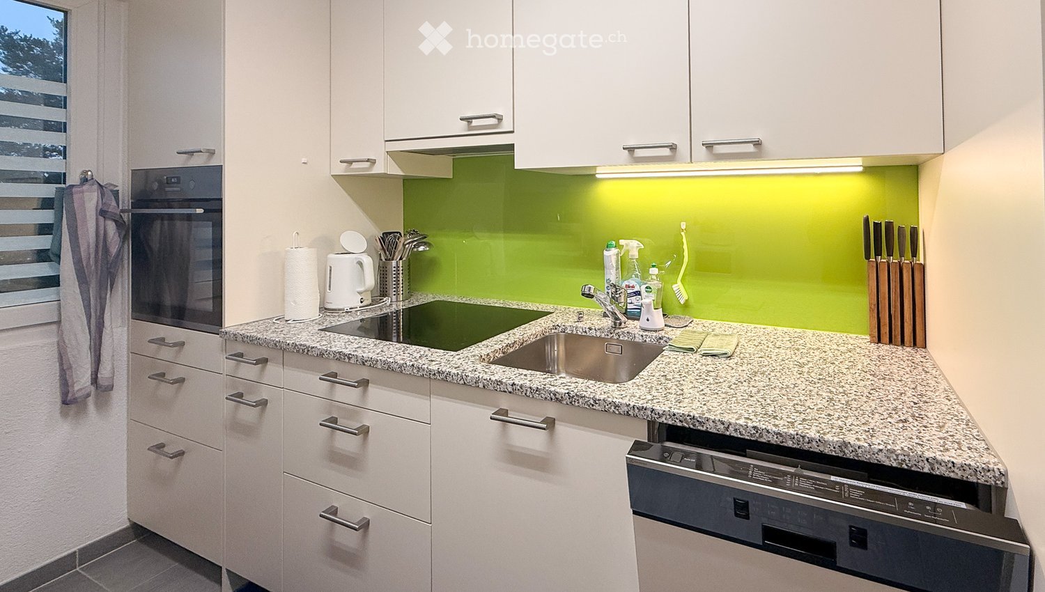 Modern kitchen with white cabinets, granite countertop, built-in oven, dishwasher, and various kitchen utensils and appliances.