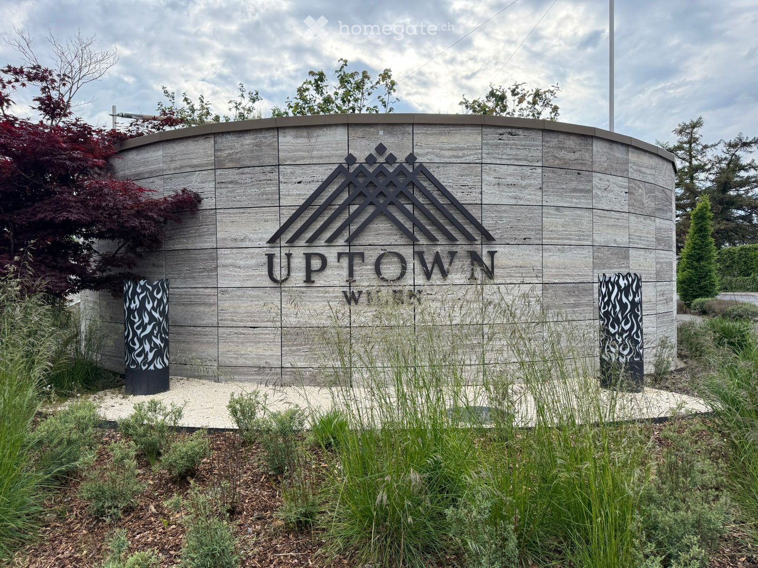 A modern sign for "Uptown" with a stylized mountain logo, surrounded by landscaped greenery and decorative columns.