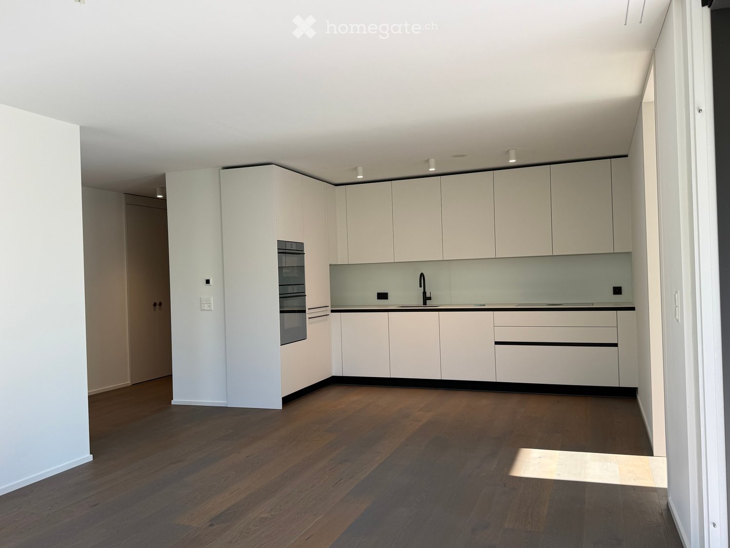 Modern kitchen with white cabinets, wooden flooring, and built-in appliances including a sink, faucet, and oven.