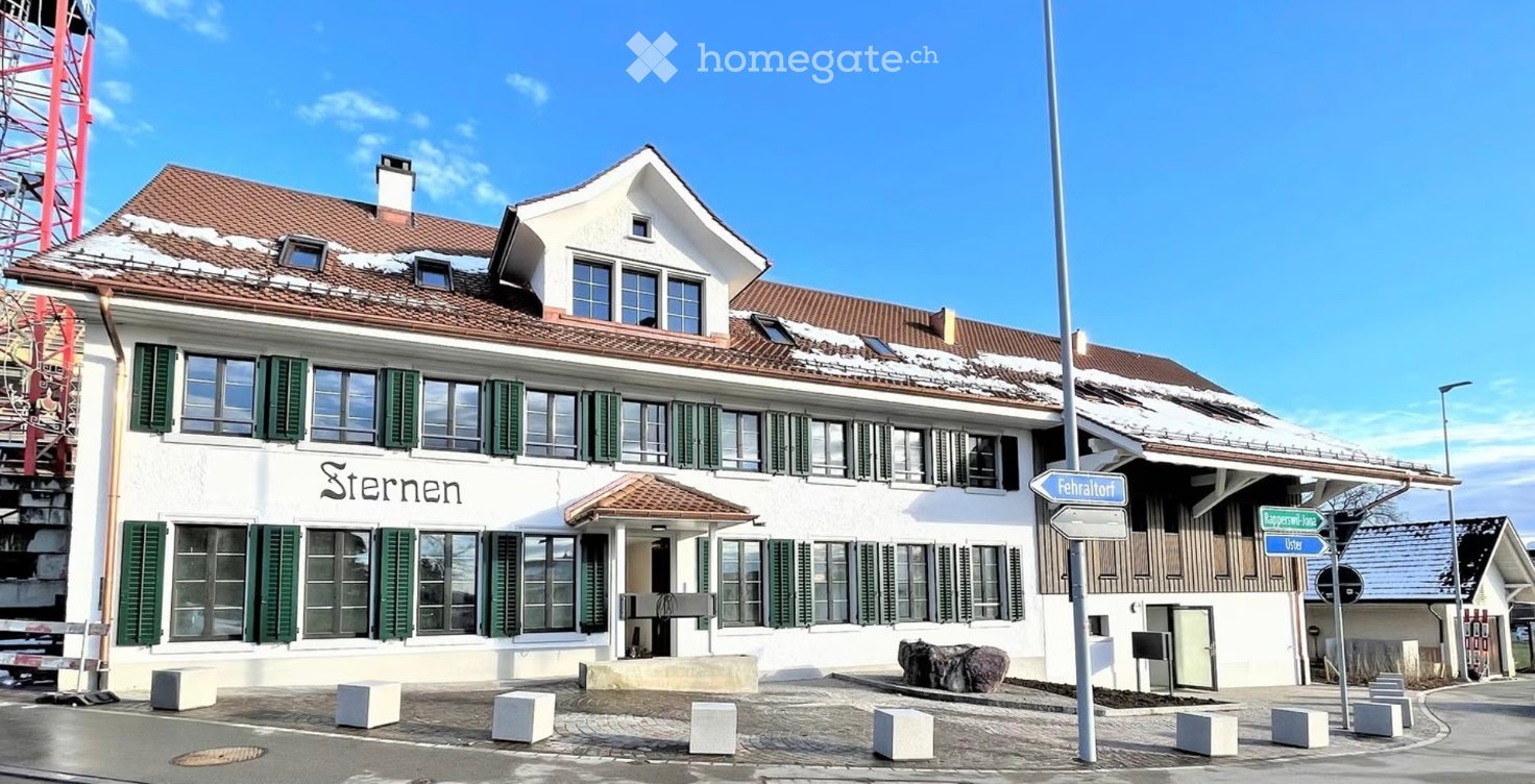 A two-story white building with green shutters and a red-tiled roof, featuring a sign that reads "Sternen" and a small entrance area.