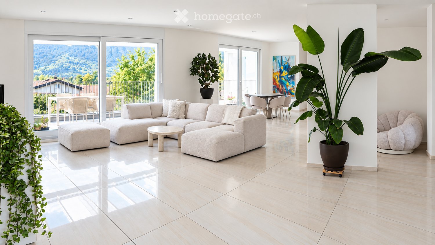 Modern living room with large windows offering a scenic view, featuring a light-colored sectional sofa, coffee table, ottoman, dining area with chairs and table, and potted plants.