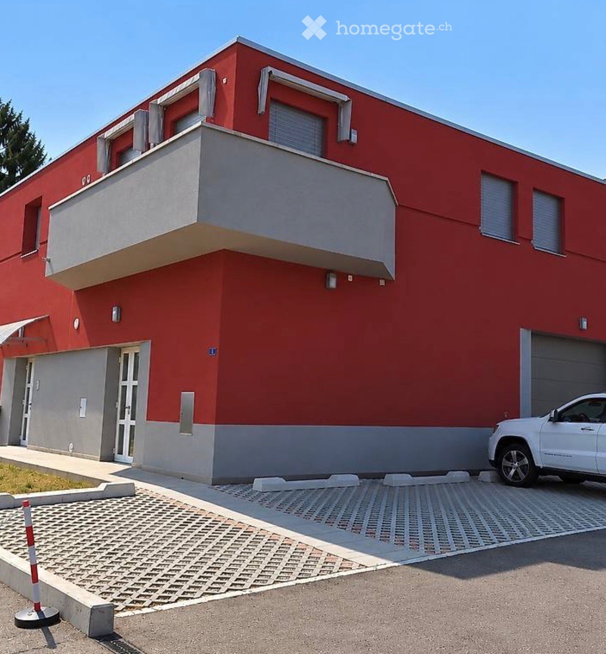 Two-story house with red brick exterior, white trim, balcony on the second floor, garage, and a paved driveway.