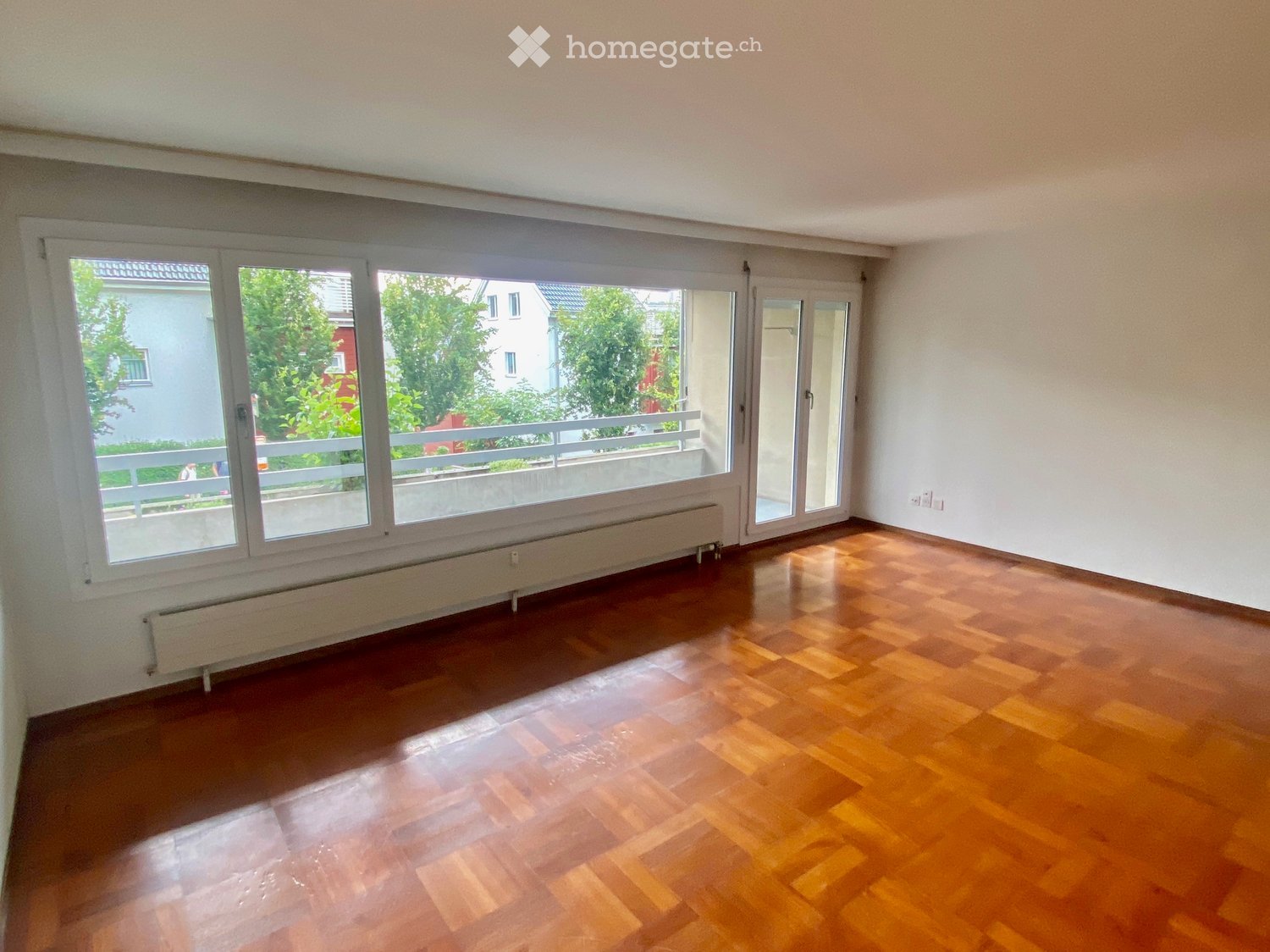 Empty room with wooden flooring, large windows, and a radiator. No furniture or equipment present.