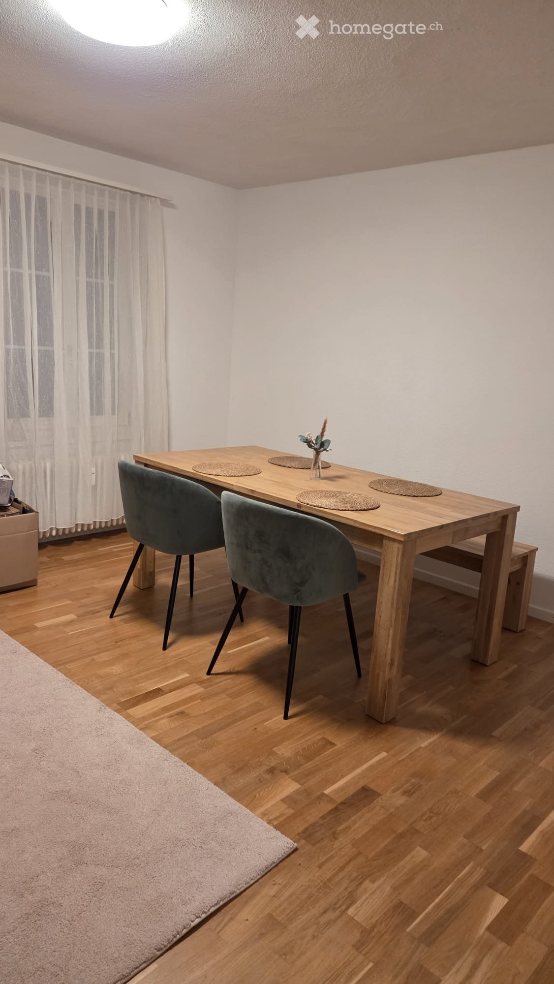 Dining room with wooden table, two grey chairs, placemats, vase with flowers, and a rug on the floor.