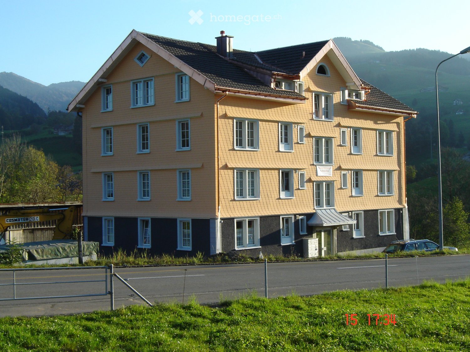 large house with yellow exterior and black roof, many windows, located on the side of the road, fenced in front