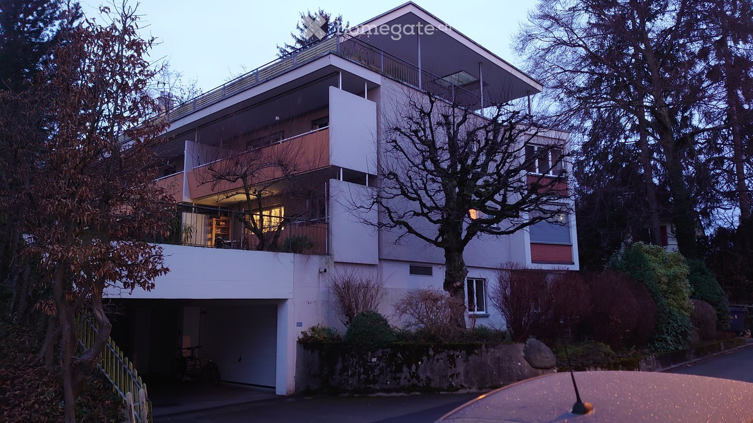 Modern multi-story building with white and red accents, large windows, balconies, and a visible garage entrance.