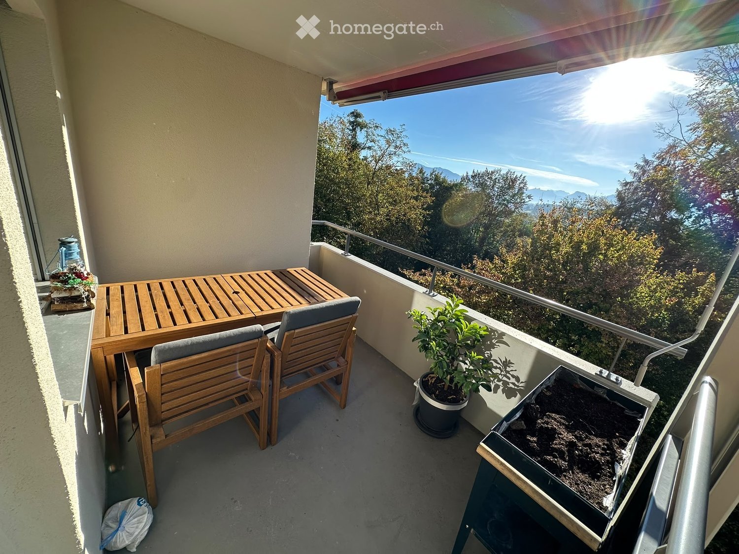 Balcony with wooden table and chairs, potted plant, scenic mountain view.