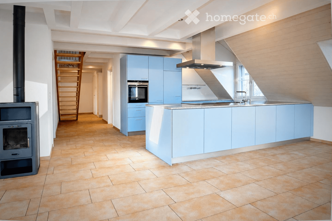 Modern kitchen with light blue cabinets, a central island, a built-in oven, a sink with a faucet, a range hood, and a wooden ladder leading to an upper level.