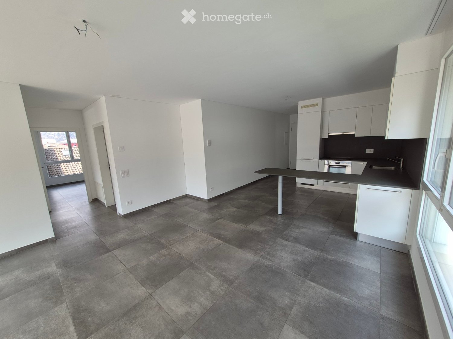 Empty kitchen with white cabinets, dark countertops, and tiled floor. No appliances or furniture present.