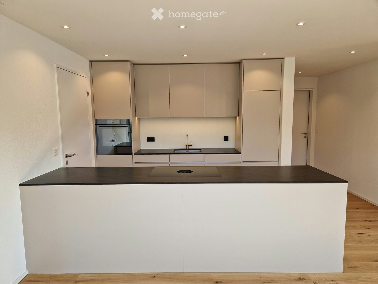 Modern kitchen with white cabinets, black countertop, built-in oven, sink, and faucet.