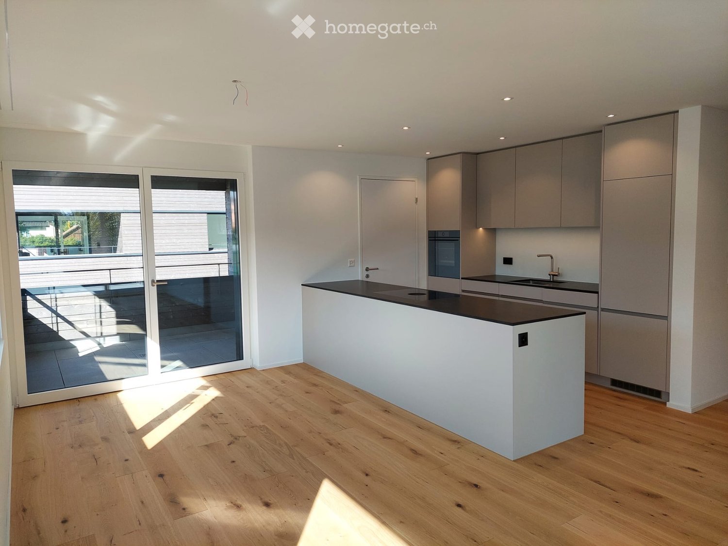 Modern kitchen with white cabinets, a central island, and a large glass door leading to a balcony.