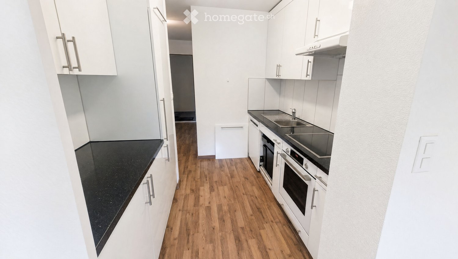 Modern kitchen with white cabinets, black countertops, and wooden flooring. Features a sink, oven, and built-in appliances.