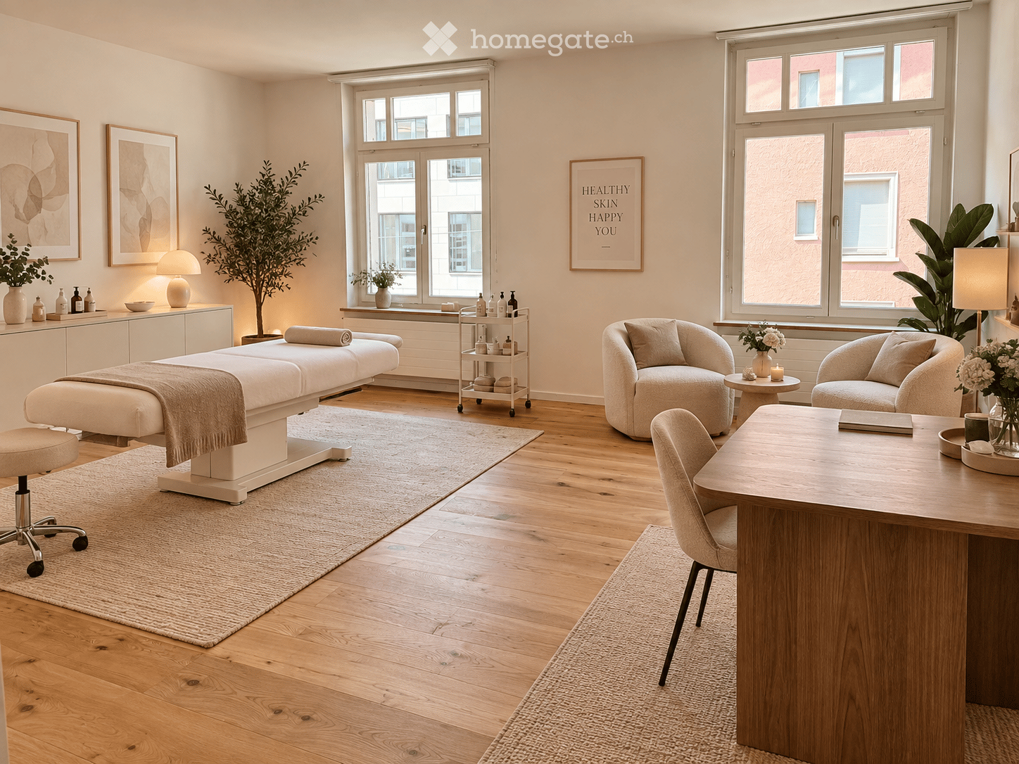 A modern, well-lit room with a massage table, two comfortable chairs, a small table, a cabinet, and decorative plants. The space features large windows, wooden flooring, and a cozy, inviting atmosphere.