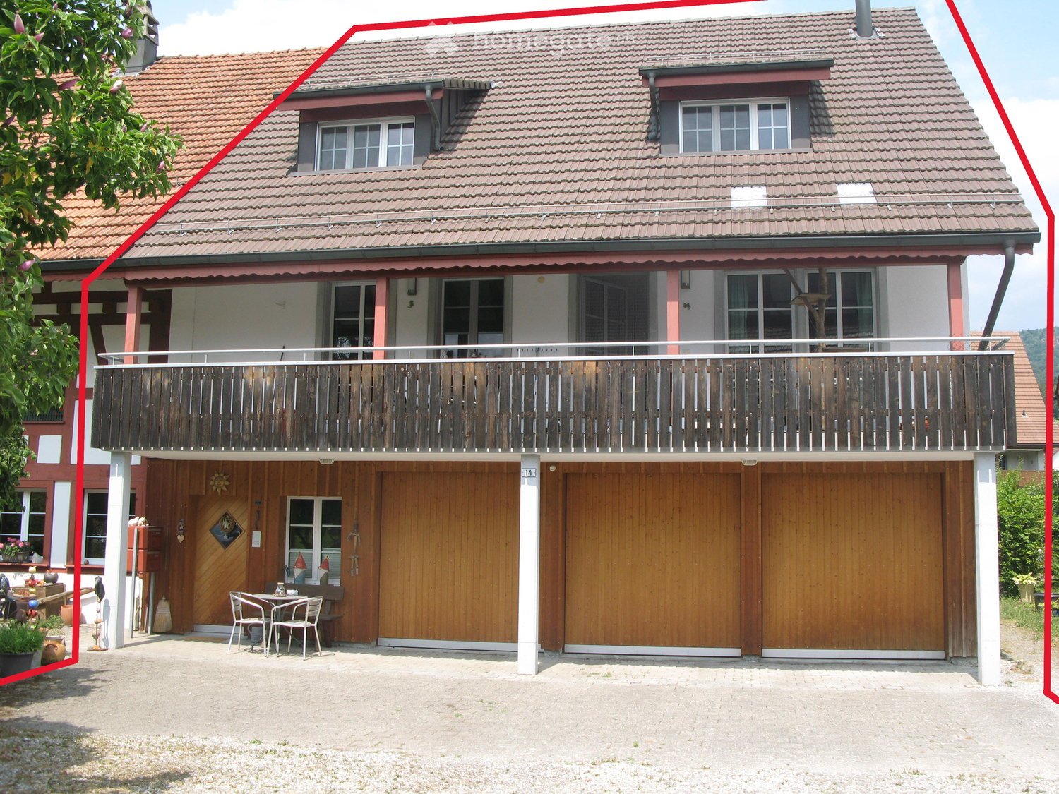 Two-story house with red-tiled roof, balcony, garage, and small outdoor seating area.