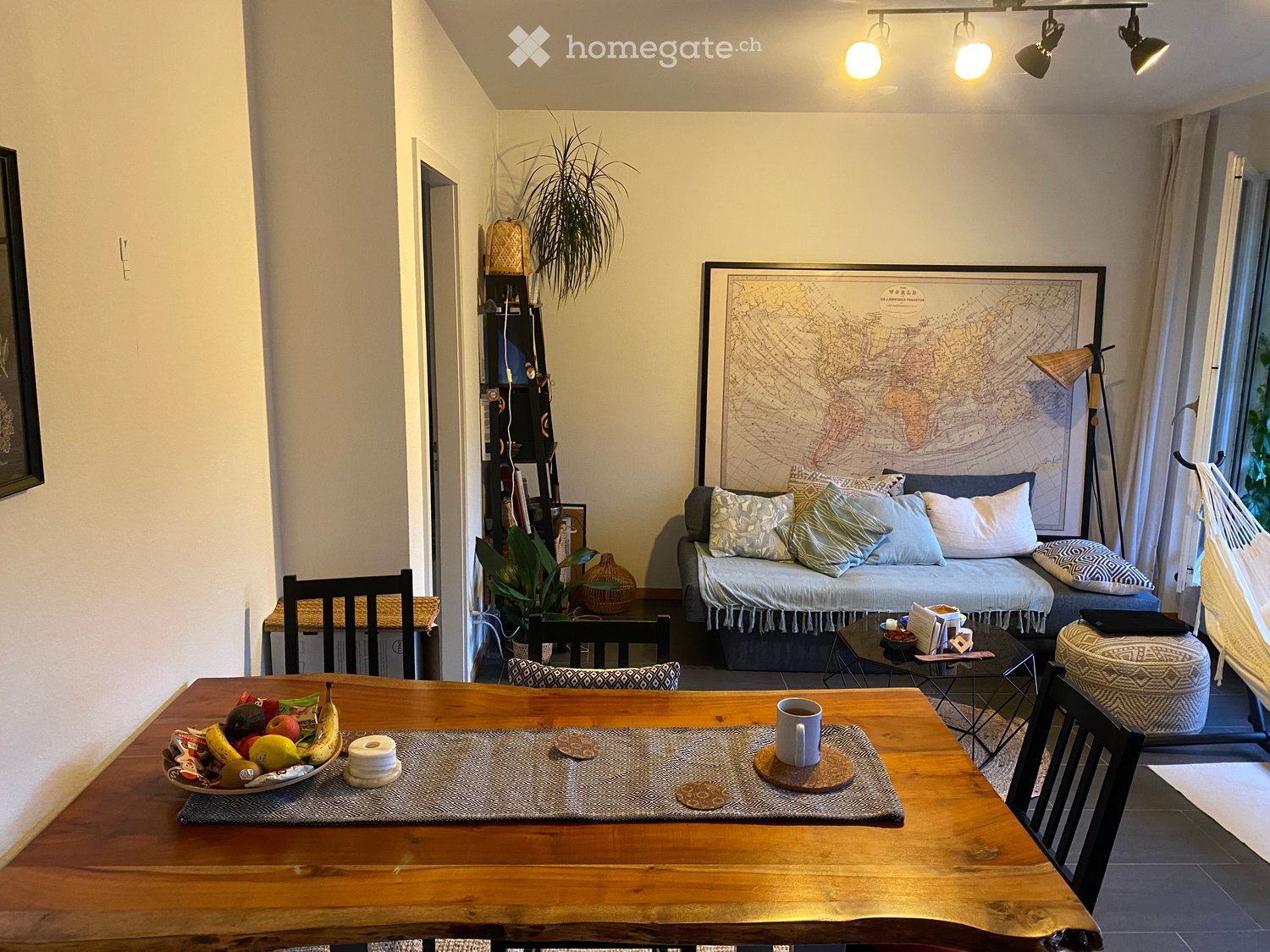 A cozy living and dining area with a wooden dining table, sofa, chairs, and decorative items including a world map and plants.
