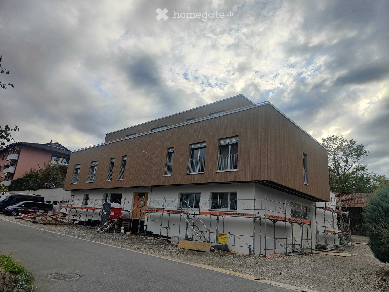 Modern two-story building under construction with wooden facade and white lower section, featuring multiple windows and a flat roof.