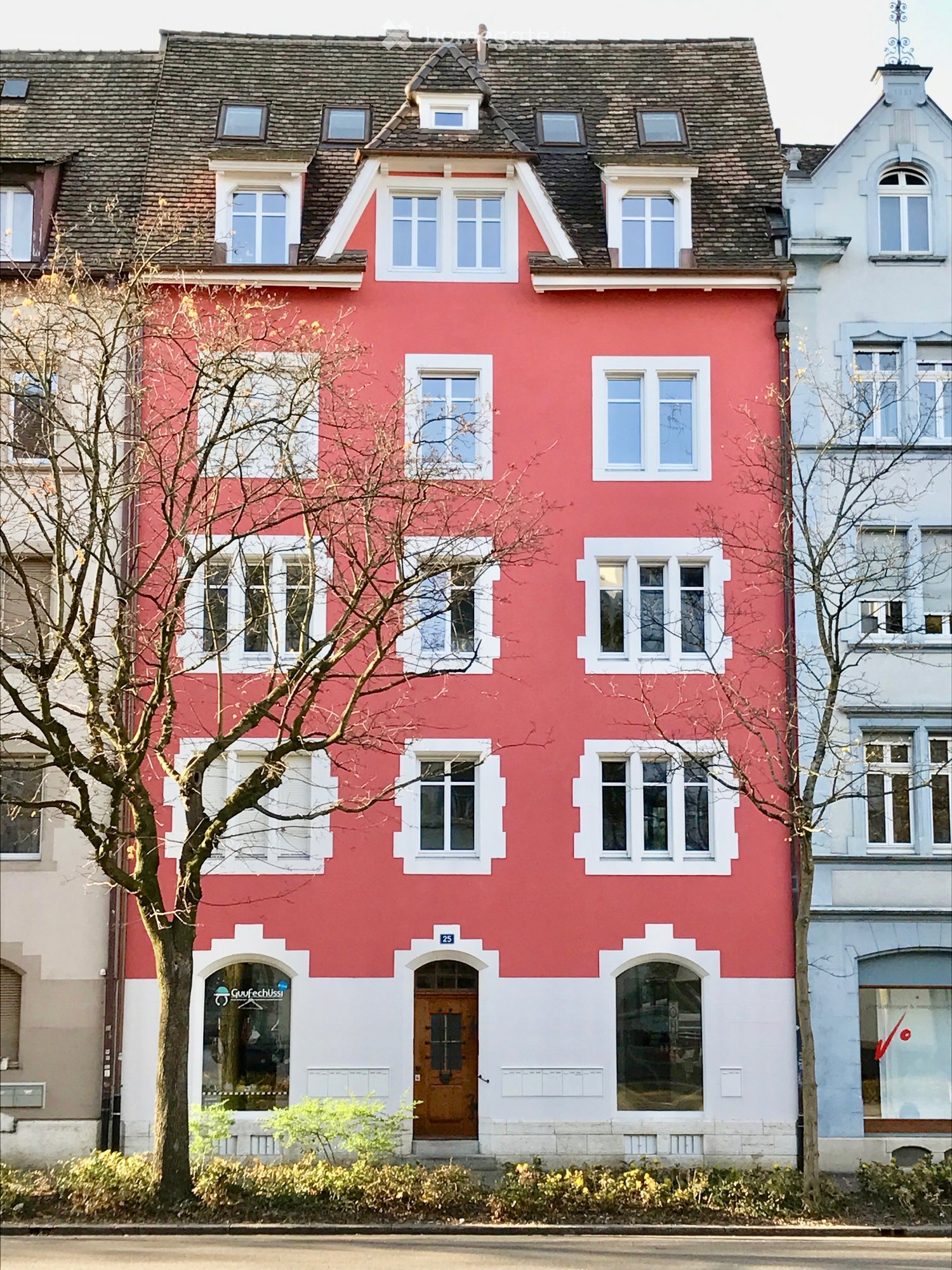 A three-story red house with white trim around the windows and doors, featuring multiple windows and a central entrance with a wooden door.