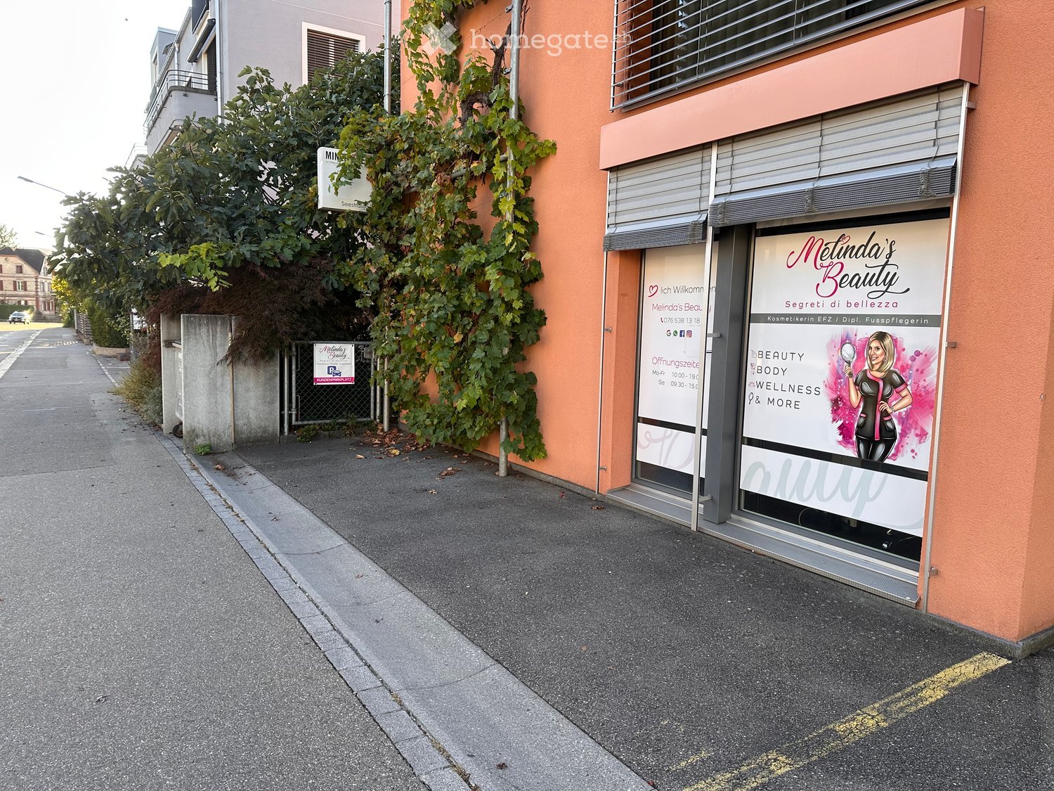 A street view showing a building with a beauty salon storefront named "Meilinda's Beauty" and a neighboring building with a sign for "Meilinda's Beauty" and a small fence.