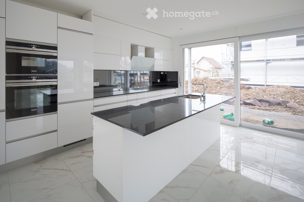 Modern kitchen with white cabinets, black countertops, built-in ovens, and a central island with a sink and faucet.
