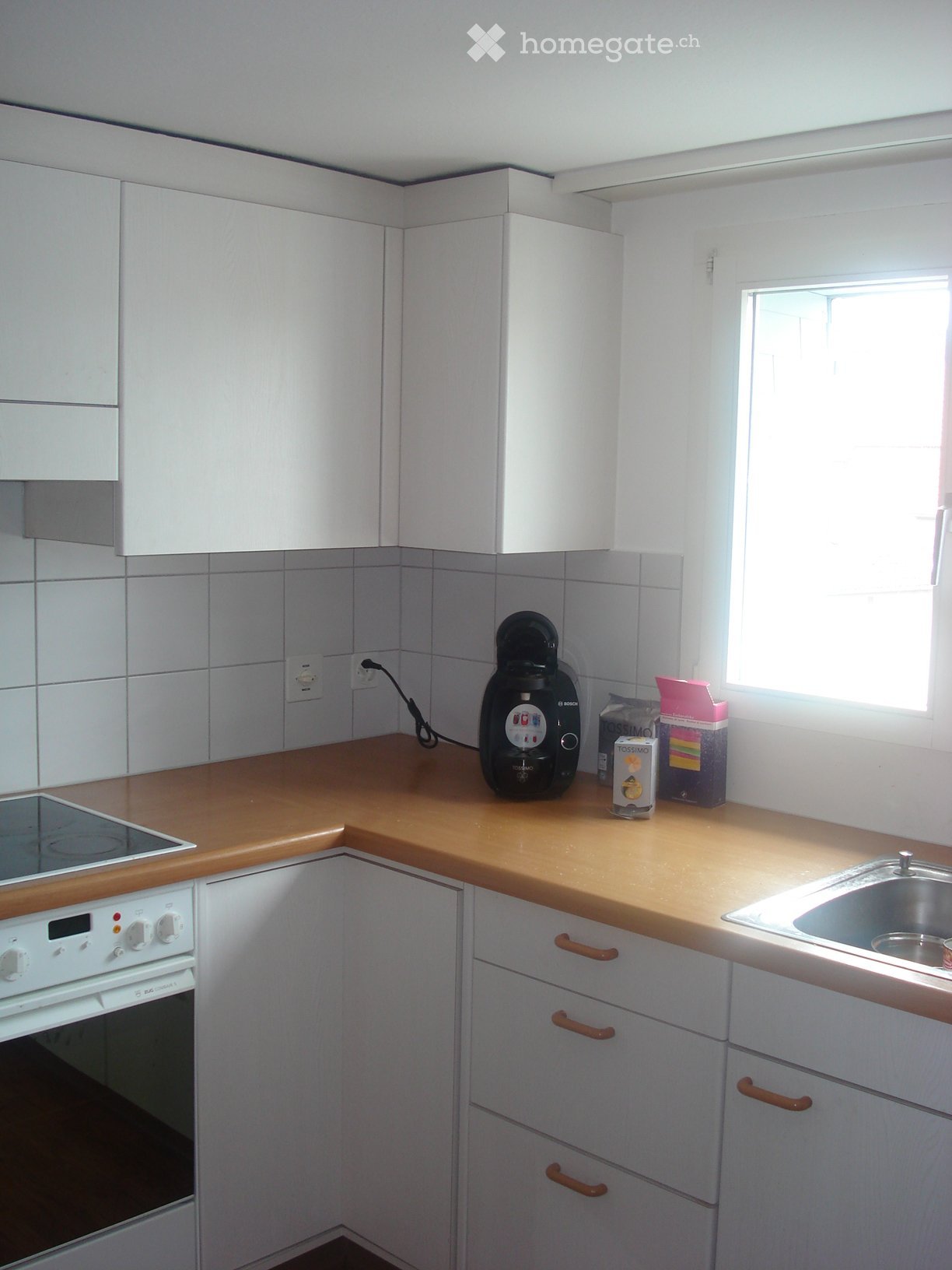 Modern kitchen with white cabinets, wooden countertops, and stainless steel sink. Features an oven, stove, and coffee maker on the counter.