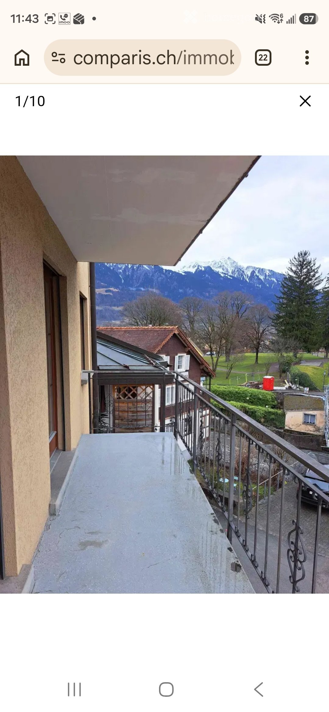 Balcony with metal railing, overlooking a scenic view of mountains and a residential area.