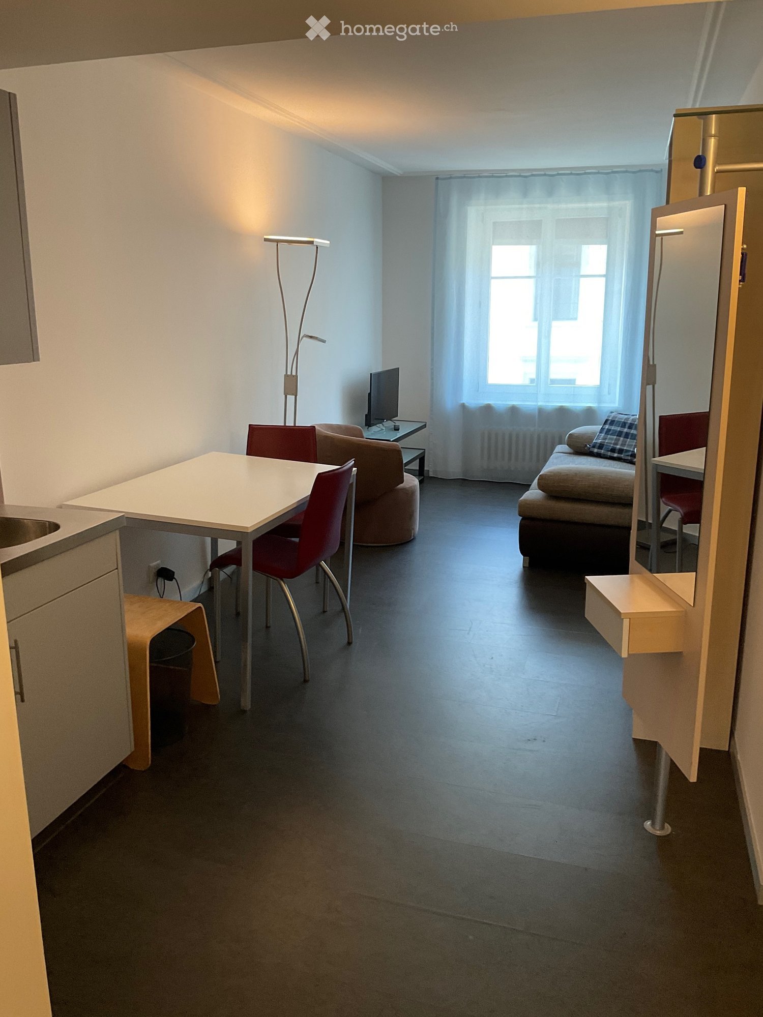 A modern, compact living space with a sofa, a small table, and chairs, featuring a large window with curtains and a sleek, contemporary design.
