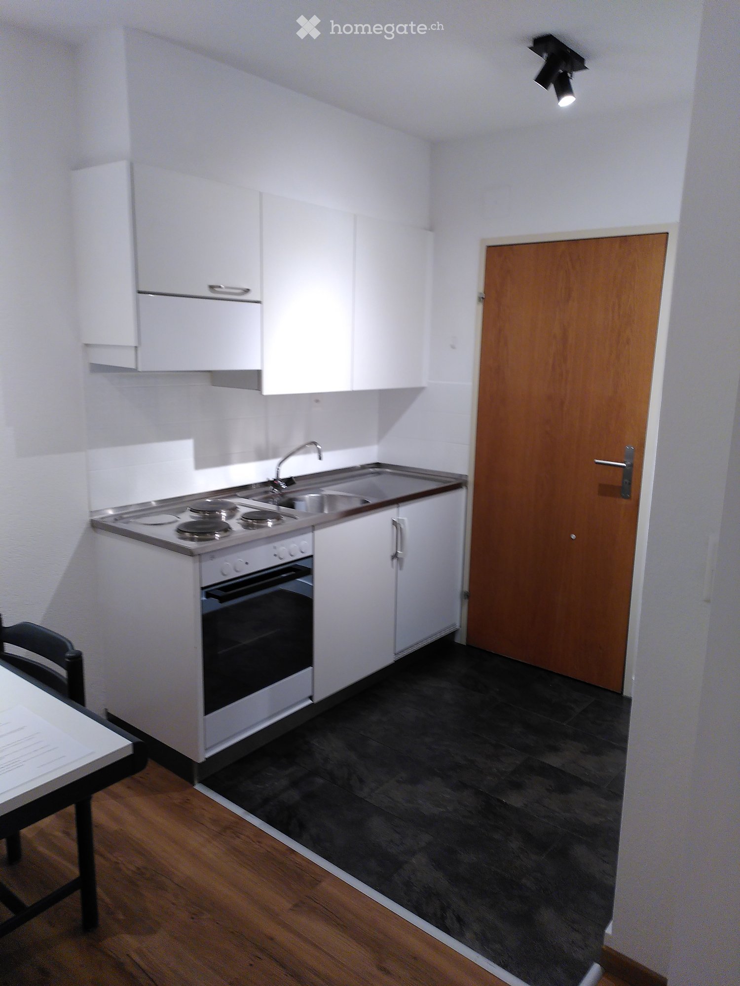 Modern kitchen with white cabinets, stainless steel stove, sink, and oven. Includes a small dining area with a table and chair.