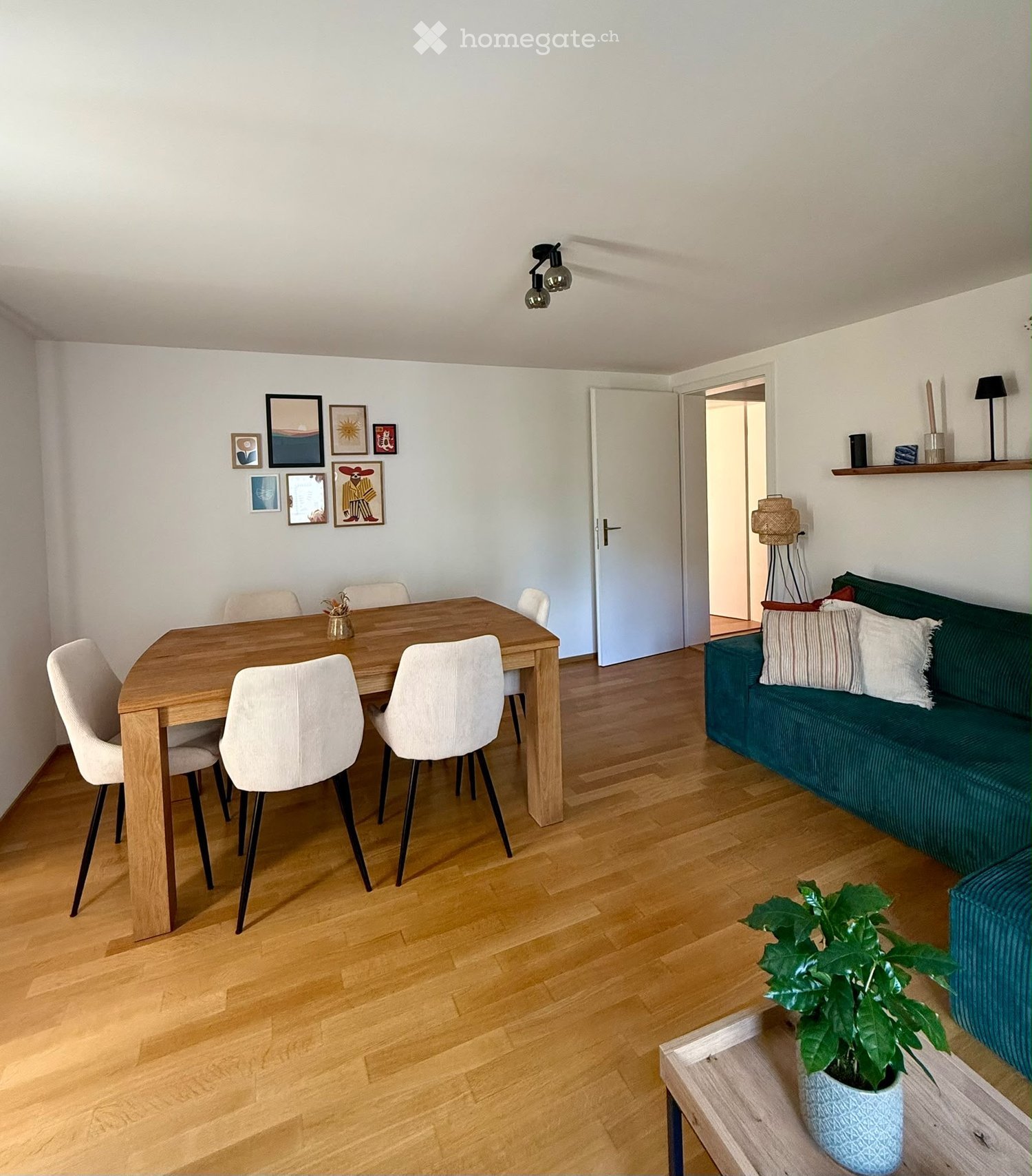 Modern living and dining area with a green sofa, wooden dining table, white chairs, and a potted plant on a side table.