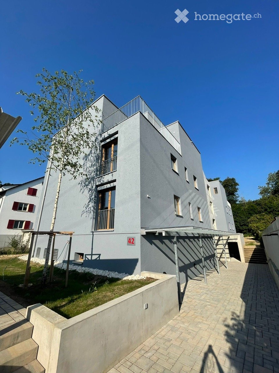 Modern two-story building with grey facade, large windows, and a balcony on the upper floor.