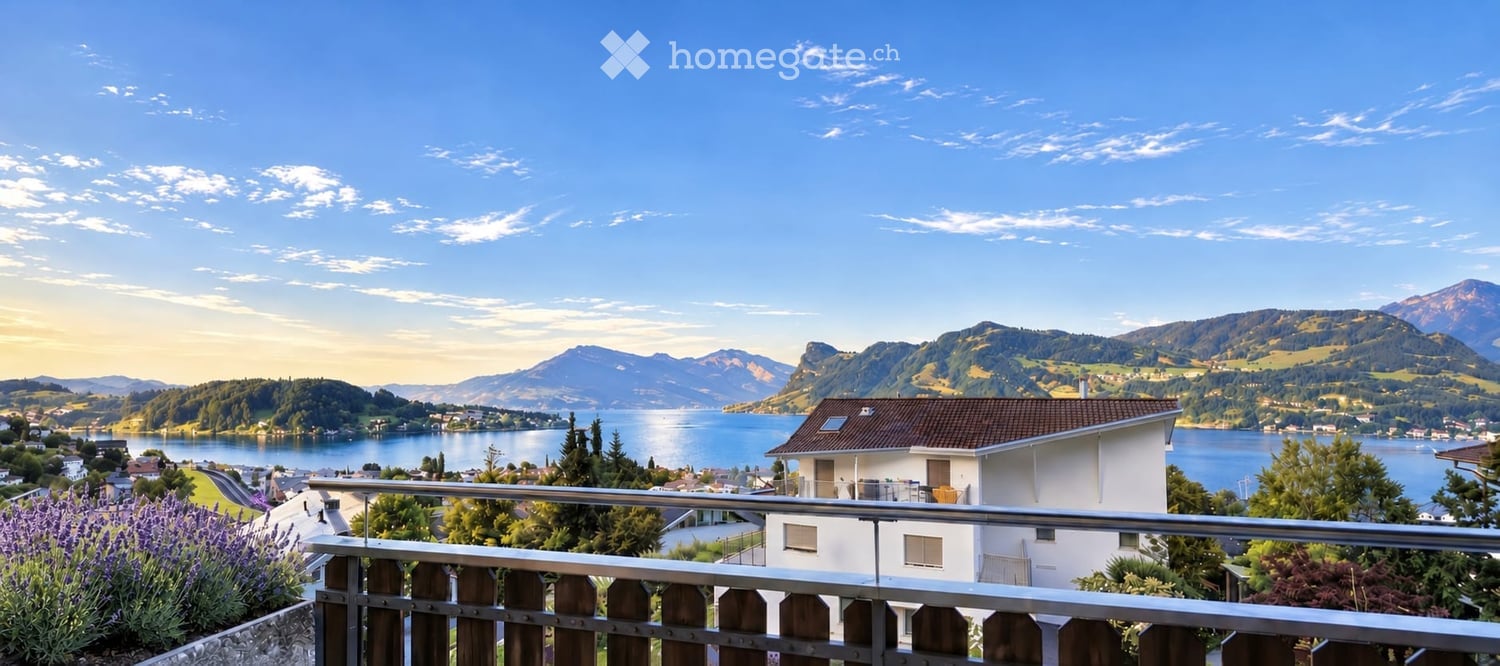 Balcony overlooking a scenic lake and mountain landscape with a white house in the foreground.