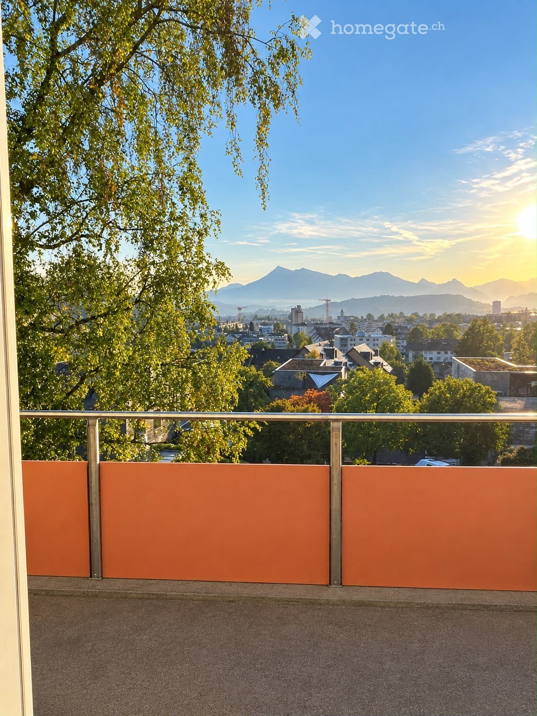 Balcony with orange privacy screens, overlooking a cityscape with trees and distant mountains.