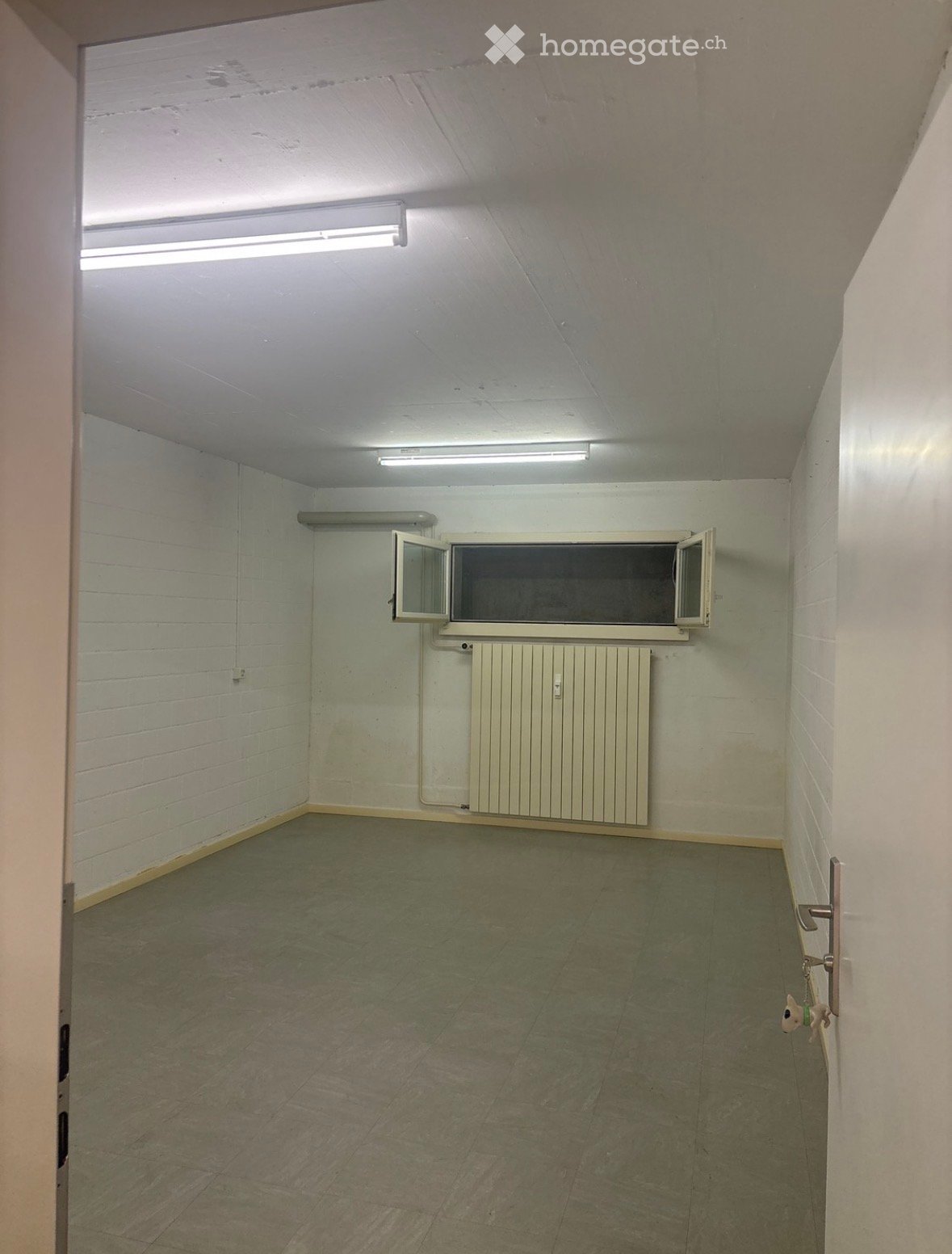 Empty room with white brick walls, concrete floor, radiator, and a small window with open shutters.