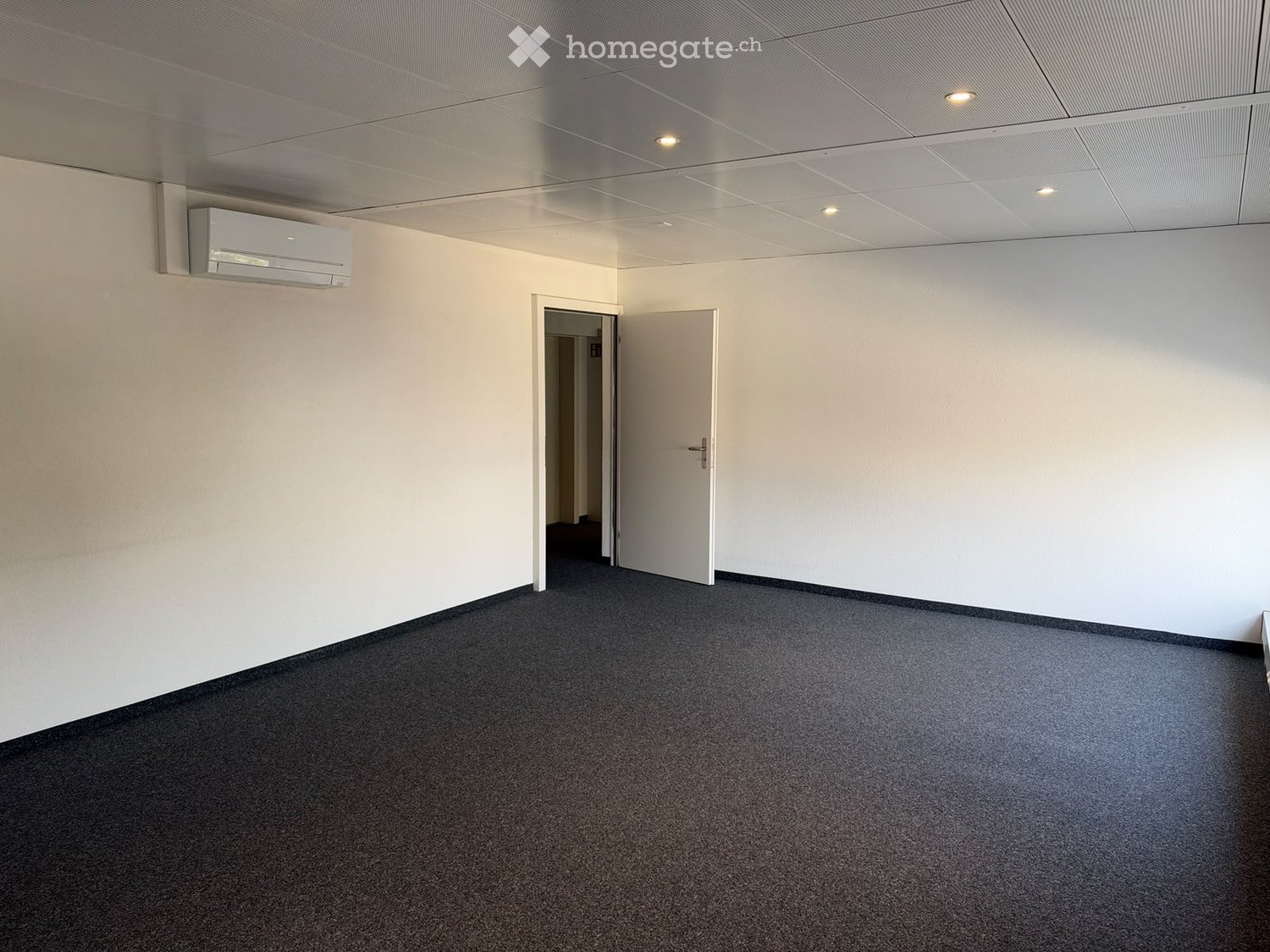 Empty room with white walls, carpeted floor, and a mounted air conditioning unit. Two open doors lead to adjacent spaces.