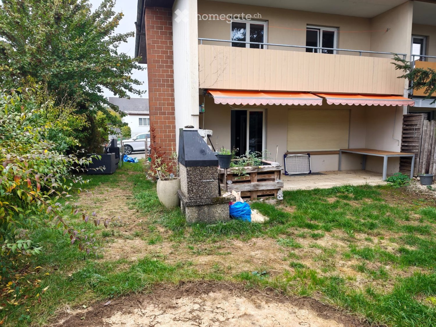 Backyard with a barbecue, patio furniture, and a covered outdoor seating area attached to a two-story house with a balcony.