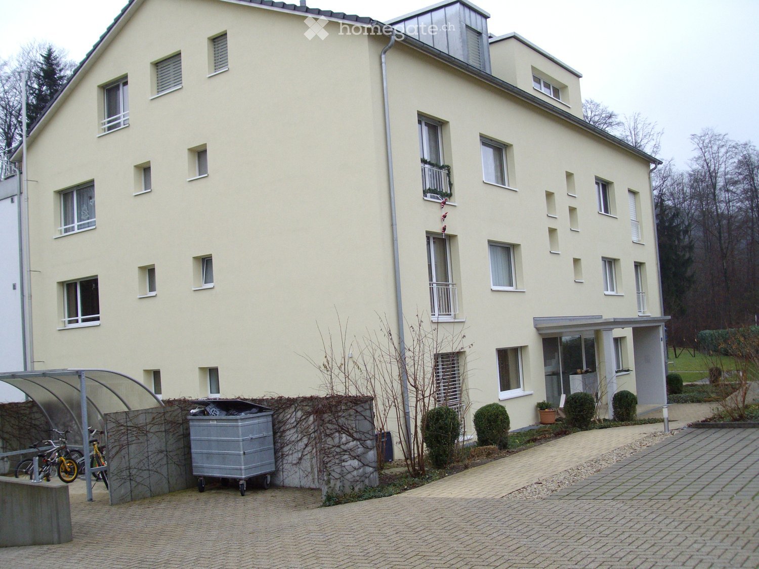 Four-story residential building with light yellow facade, multiple windows, balconies, and a covered entrance area.