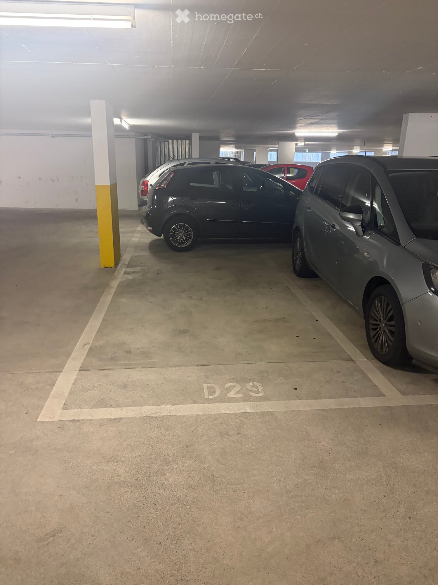 Underground parking area with several parked cars, marked parking spaces, and concrete pillars.