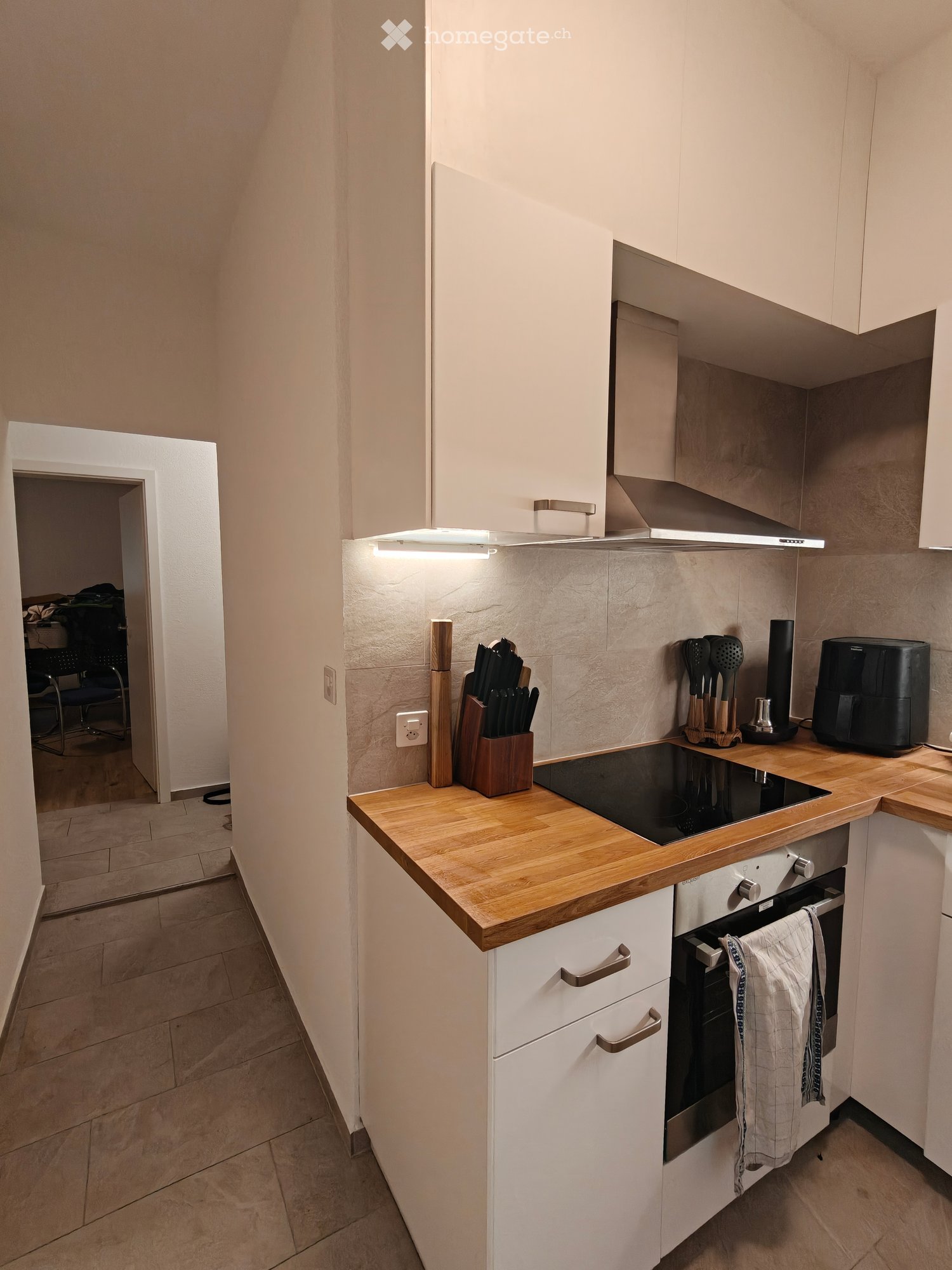 Modern kitchen with white cabinets, wooden countertops, induction stove, oven, knife block, frying pan, oven mitt, air fryer, and a towel hanging on the oven handle.