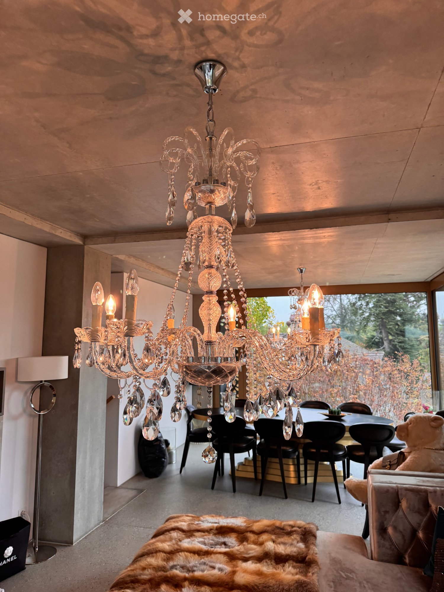 Modern living and dining area with a large chandelier, sofa, dining table, chairs, and a fur throw on the sofa.