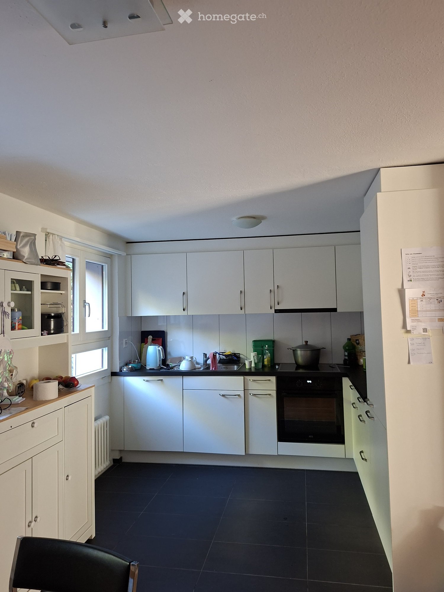 Modern kitchen with white cabinets, black countertops, and stainless steel appliances. Includes a refrigerator, oven, sink, and various kitchen items on the counter.