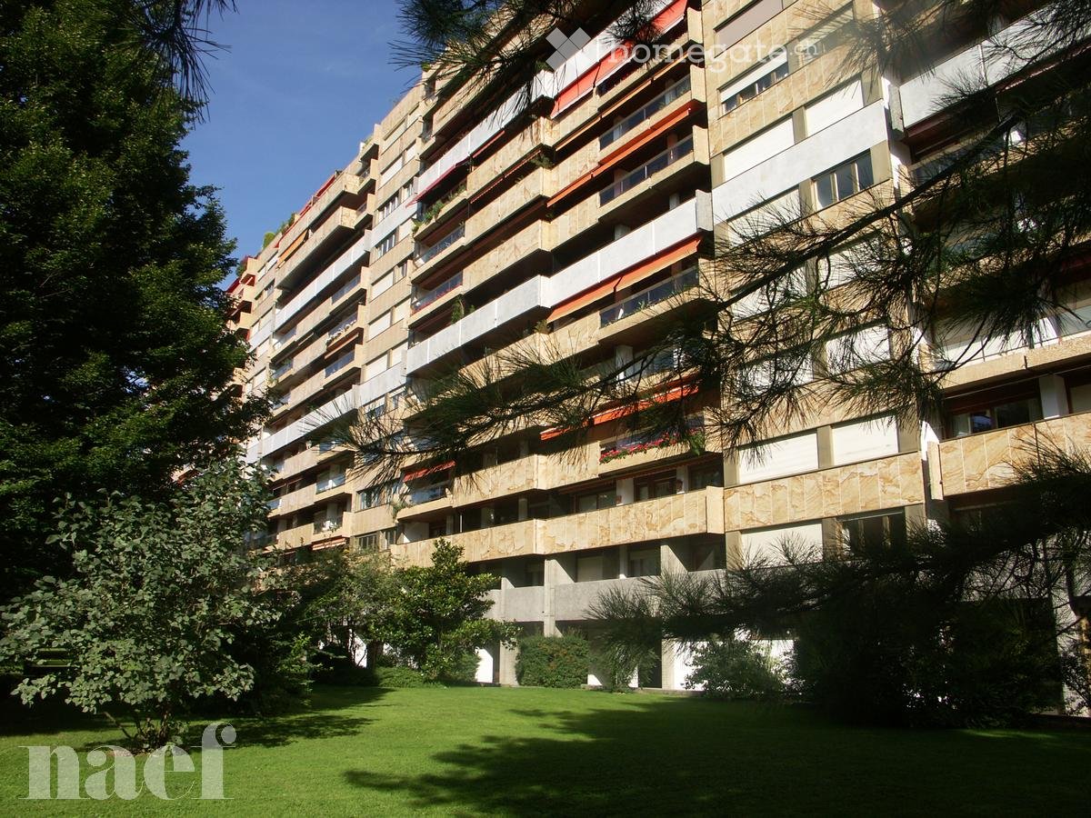 A multi-story residential building with balconies and greenery in the foreground.