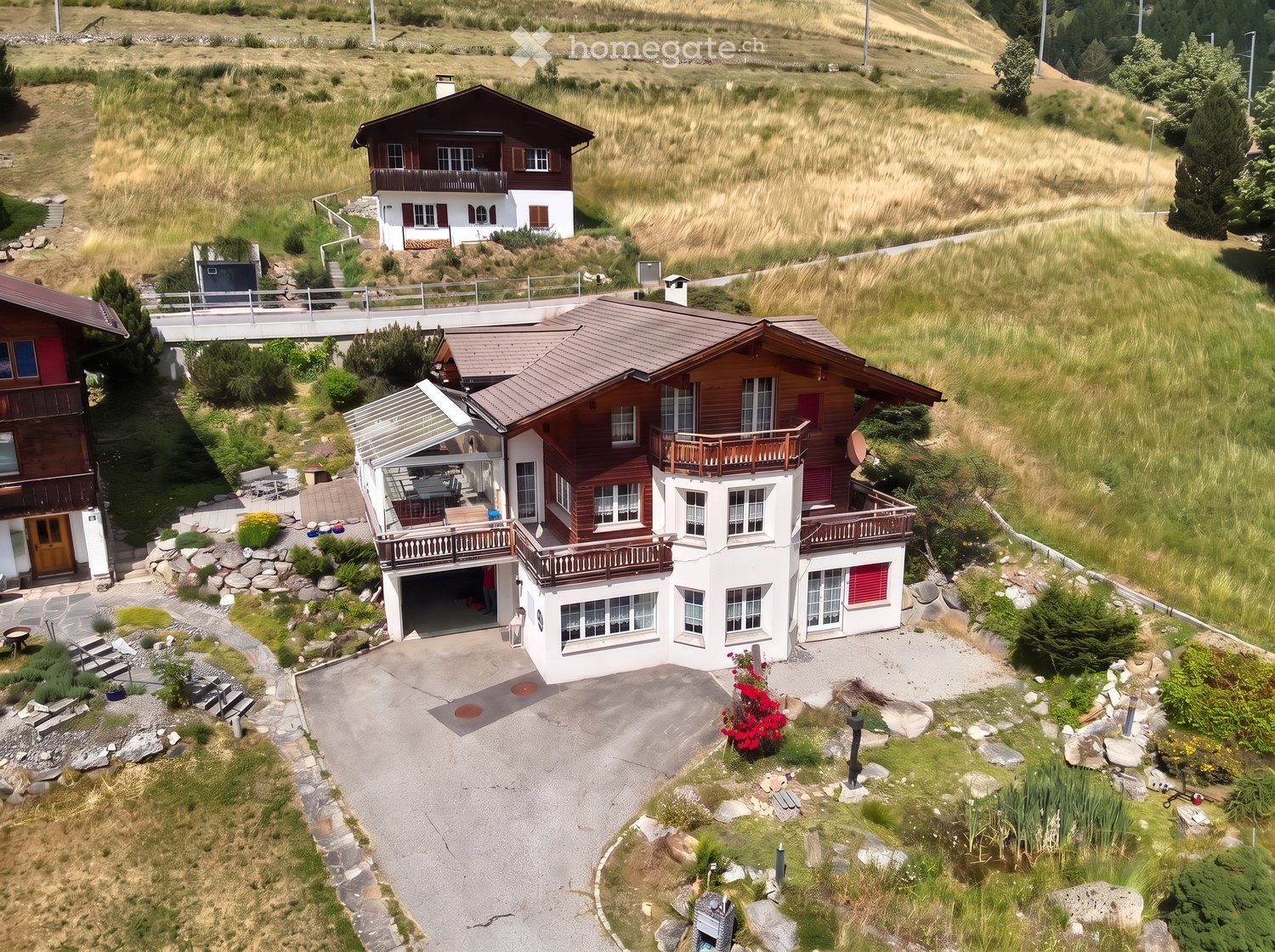 Aerial view of a two-story house with a garage, balconies, and a well-maintained garden in a rural setting.