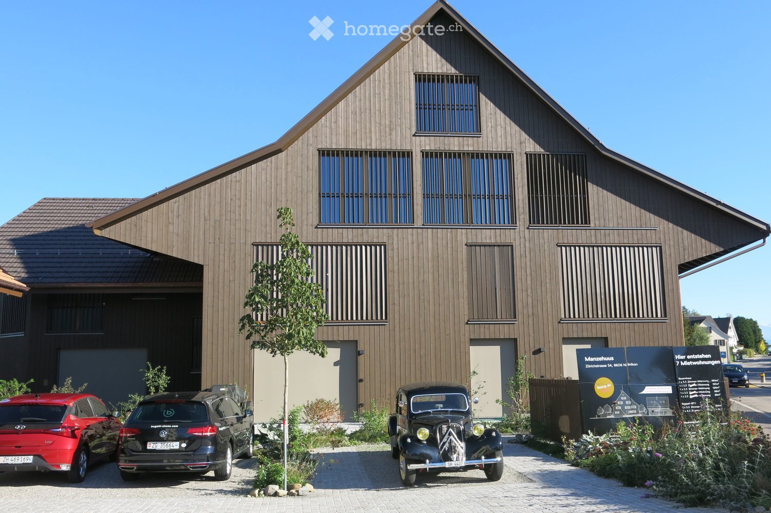 Modern two-story house with wooden exterior, large windows, and a garage. Features a sloped roof and contemporary design.