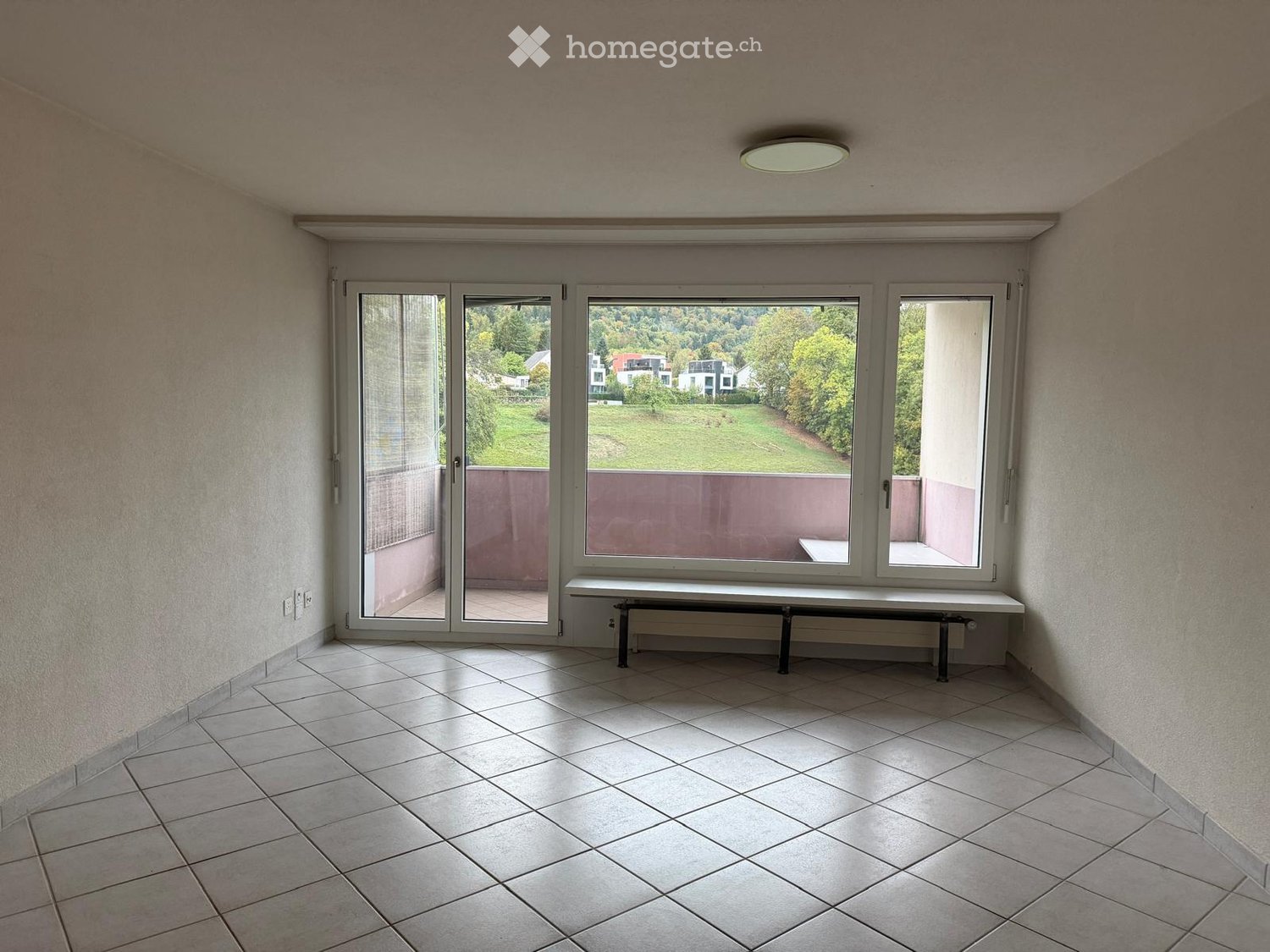 Empty room with tiled floor, large windows, and a bench beneath the windows.