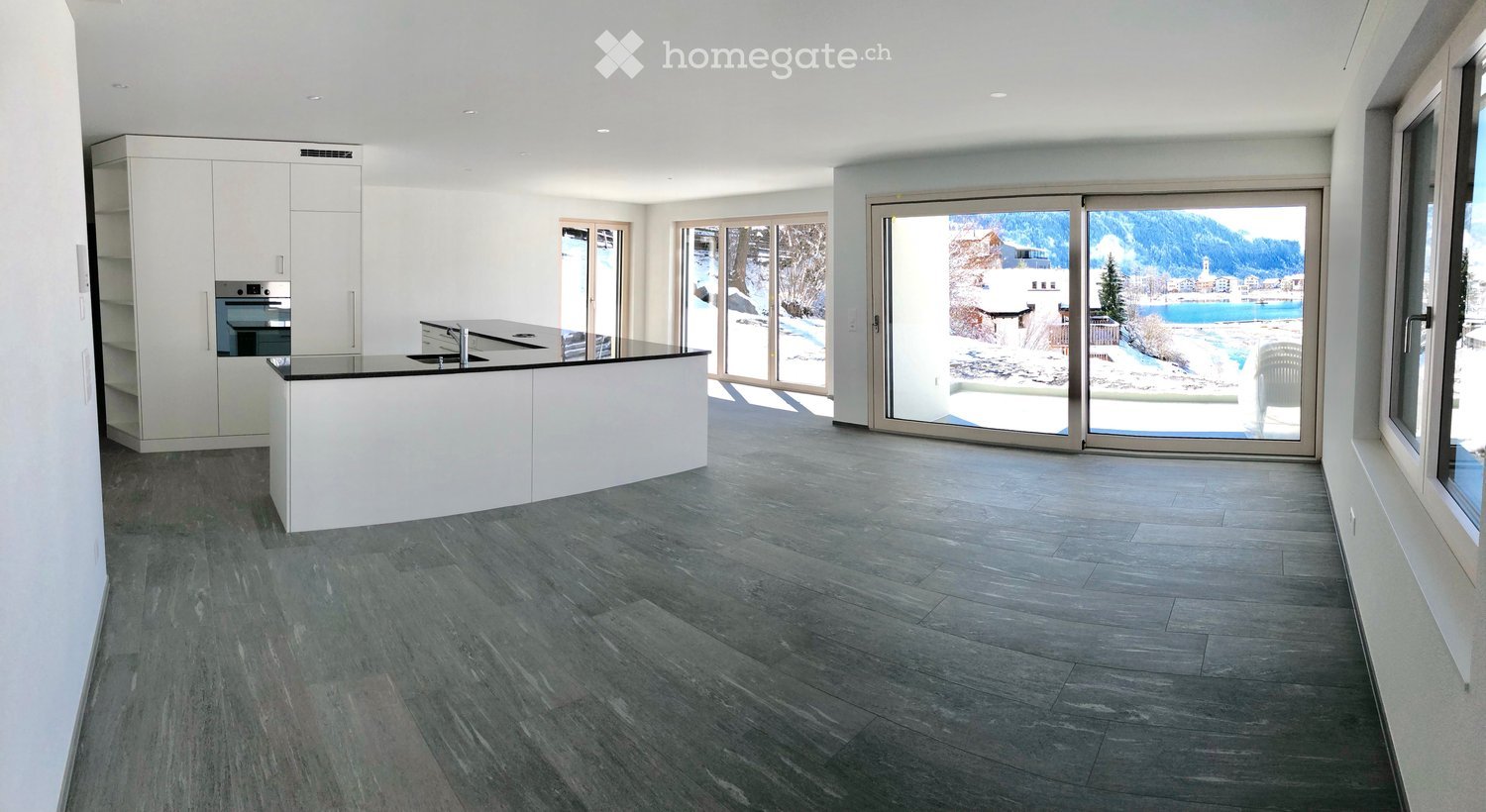 Furnished Room. Modern kitchen with a large island, white cabinets, and a view of a snowy landscape.
