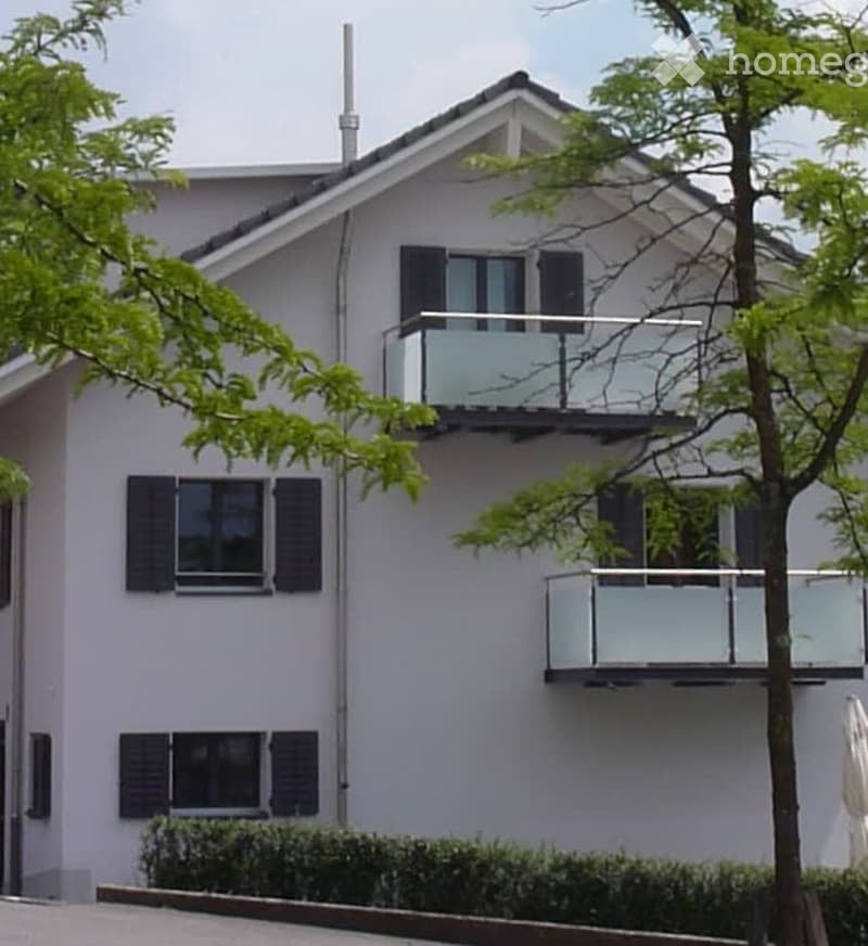 Modern two-story house with white exterior, black shutters, and multiple balconies with glass railings.